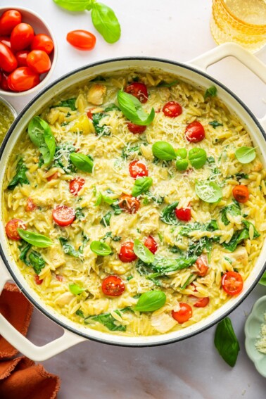A large pot of pesto chicken, orzo, cherry tomatoes, spinach, parmesan cheese, and fresh basil.