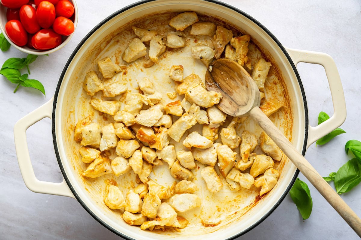 Chicken chunks being cooked in a large pot with a wooden spoon.