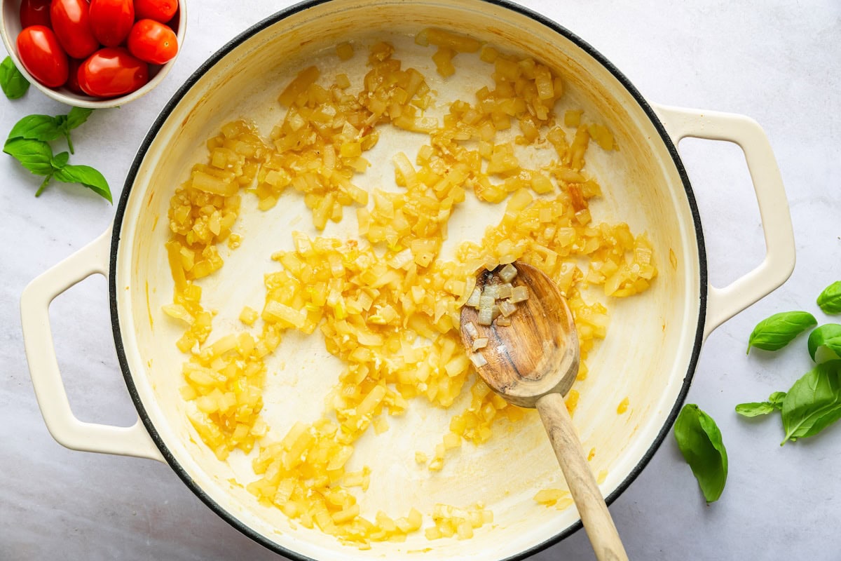 Sauteed onion in a large pot with a wooden spoon.