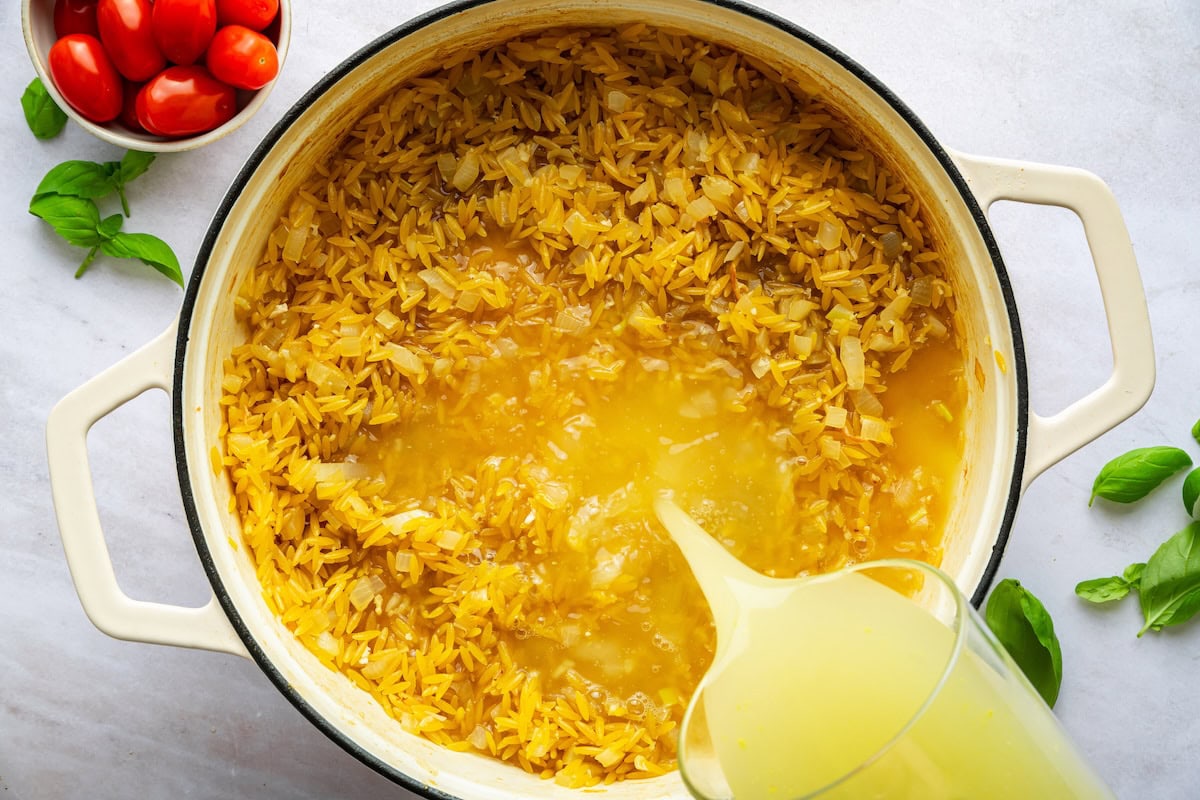 Chicken broth added to a large pot of orzo and sauteed onion.