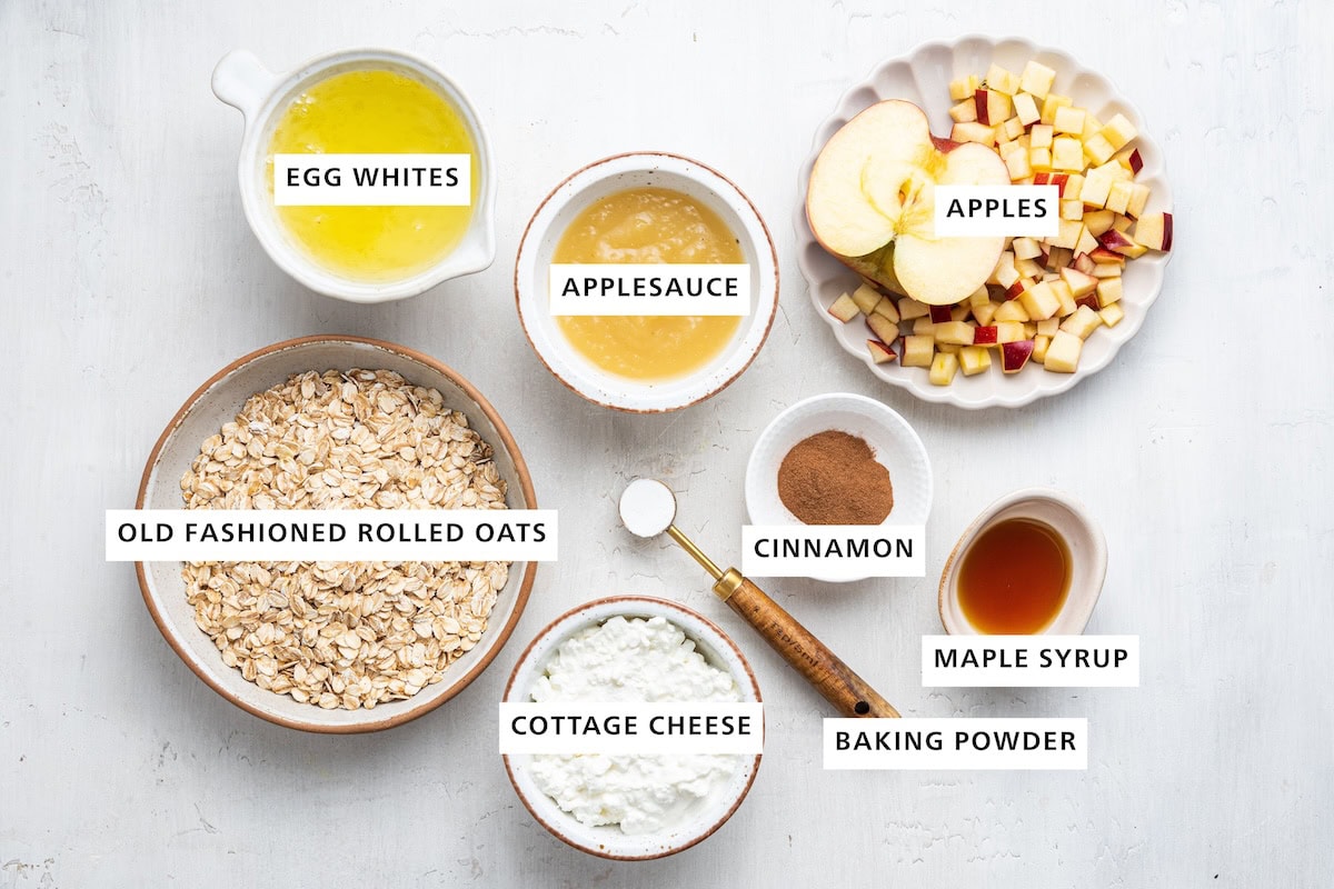 Ingredients measured out to make Healthy Apple Pancakes: oats, egg whites, cottage cheese, applesauce, baking powder, cinnamon, maple syrup and apple.
