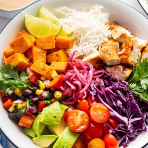 BBQ chicken bowl with white rice, chicken chunks, roasted sweet potatoes, avocado, cherry tomatoes, cabbage, pickled onions and corn and bean salad.