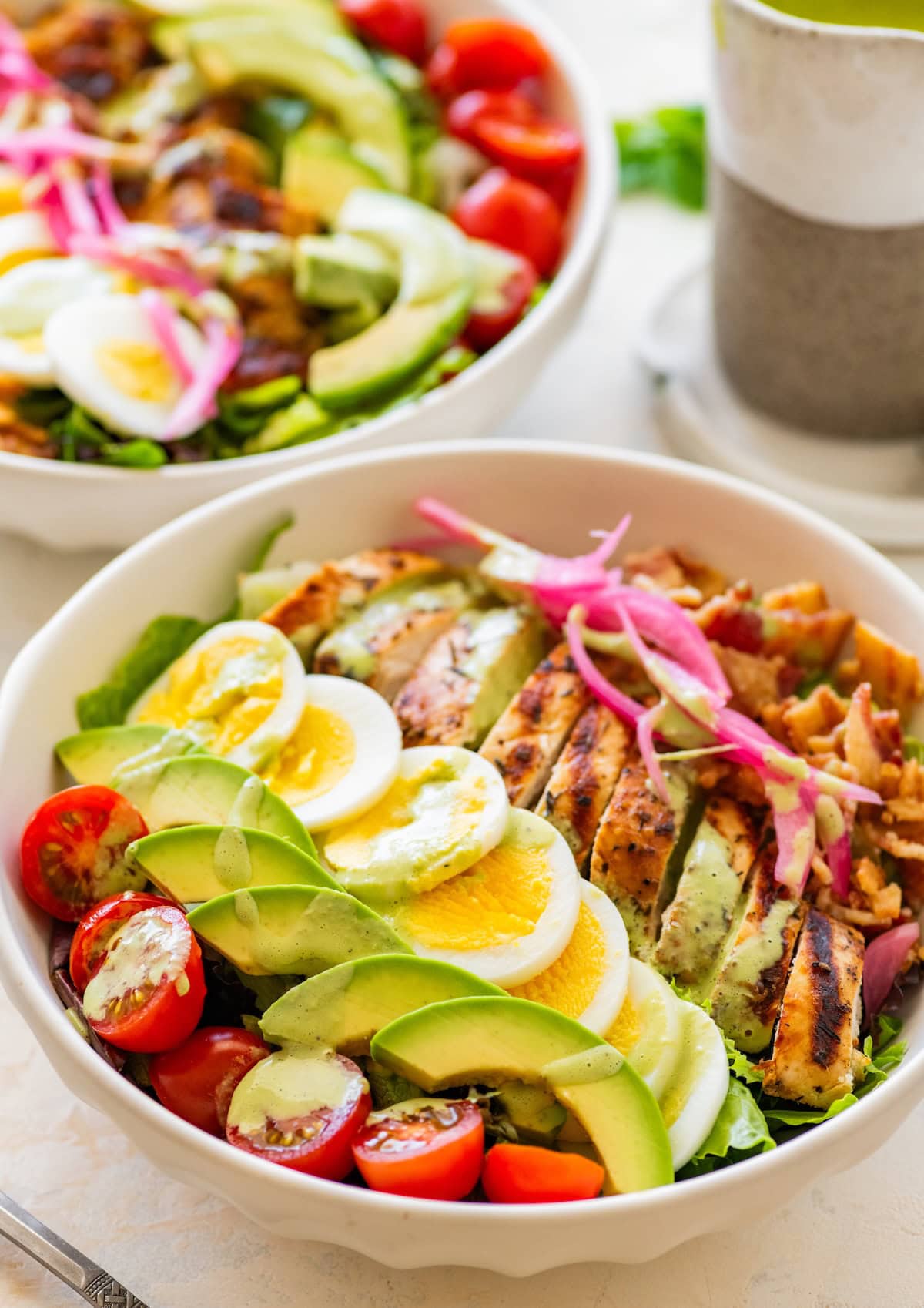 Chicken cobb salad served in a bowl with fresh veggies and a green dressing.