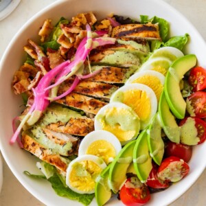 A chicken cobb salad with hard boiled egg, avocado, tomatoes, bacon, and onion in a bowl.