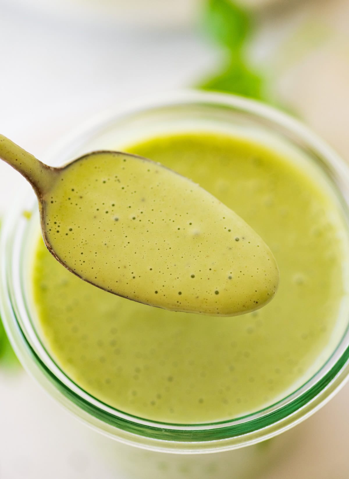 A spoonful of green goddess dressing over a glass jar of the dressing.