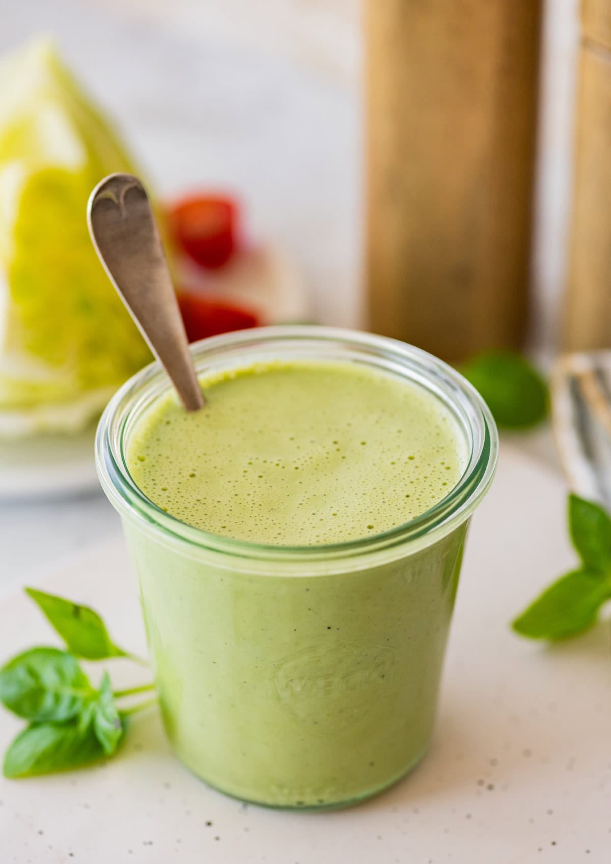A full glass jar of green goddess dressing with a metal spoon in the jar.