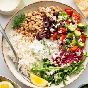 A ground turkey Greek bowl with rice, fresh vegetables, and a lemon wedge.