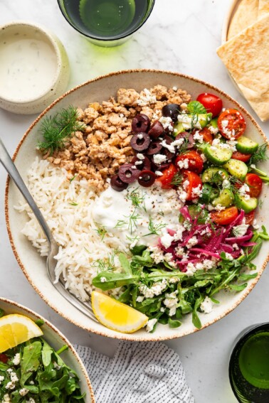 A ground turkey Greek bowl with rice, fresh vegetables, and a lemon wedge.
