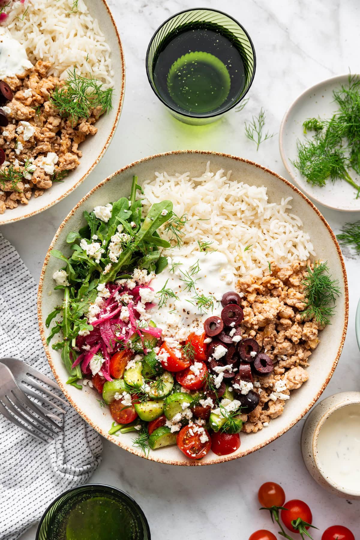 A serving of a ground turkey Greek bowl in a white bowl with fresh vegetables.