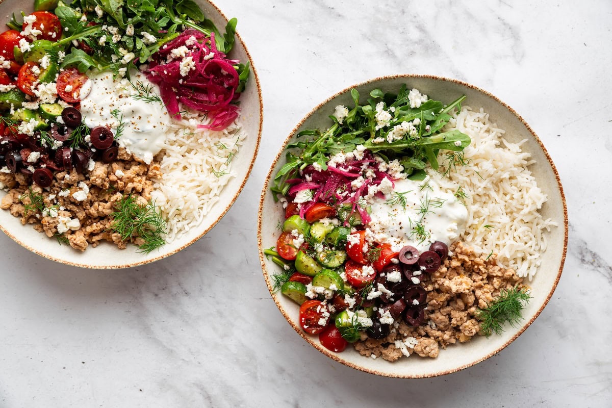 Two bowls served with cooked ground turkey, fresh vegetables, rice, and a scoop of tzatziki.