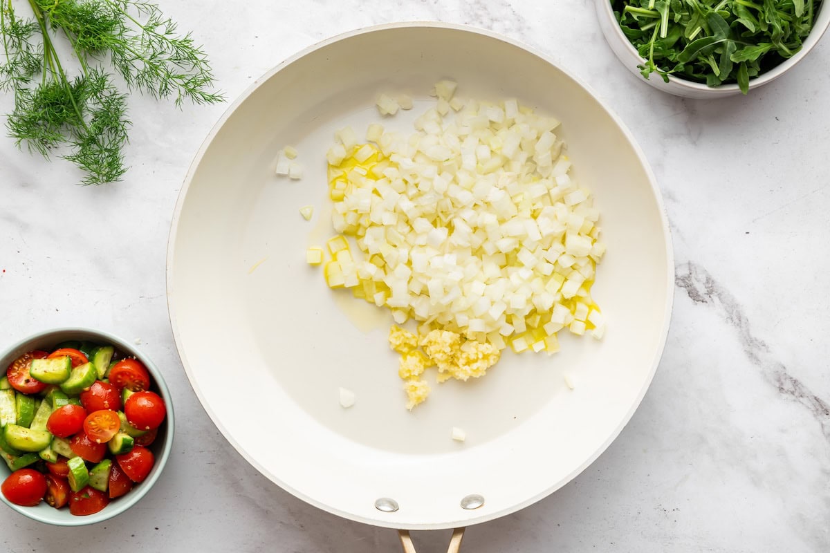 Onion and garlic sauteeing in a white skillet.
