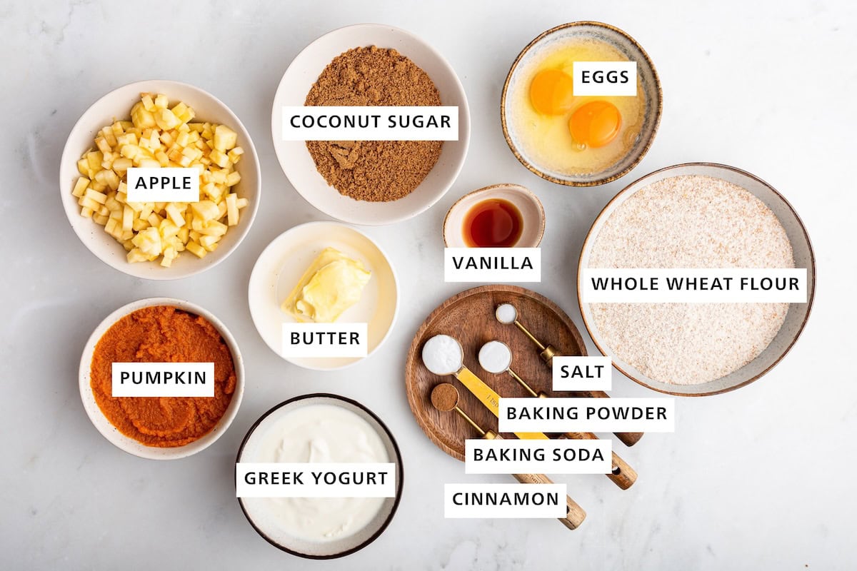 Ingredients measured out to make Healthy Apple Cinnamon Muffins: whole wheat flour, eggs, vanilla, sea salt, baking powder, cinnamon, baking soda, coconut sugar, butter, Greek yogurt, apple and pumpkin.