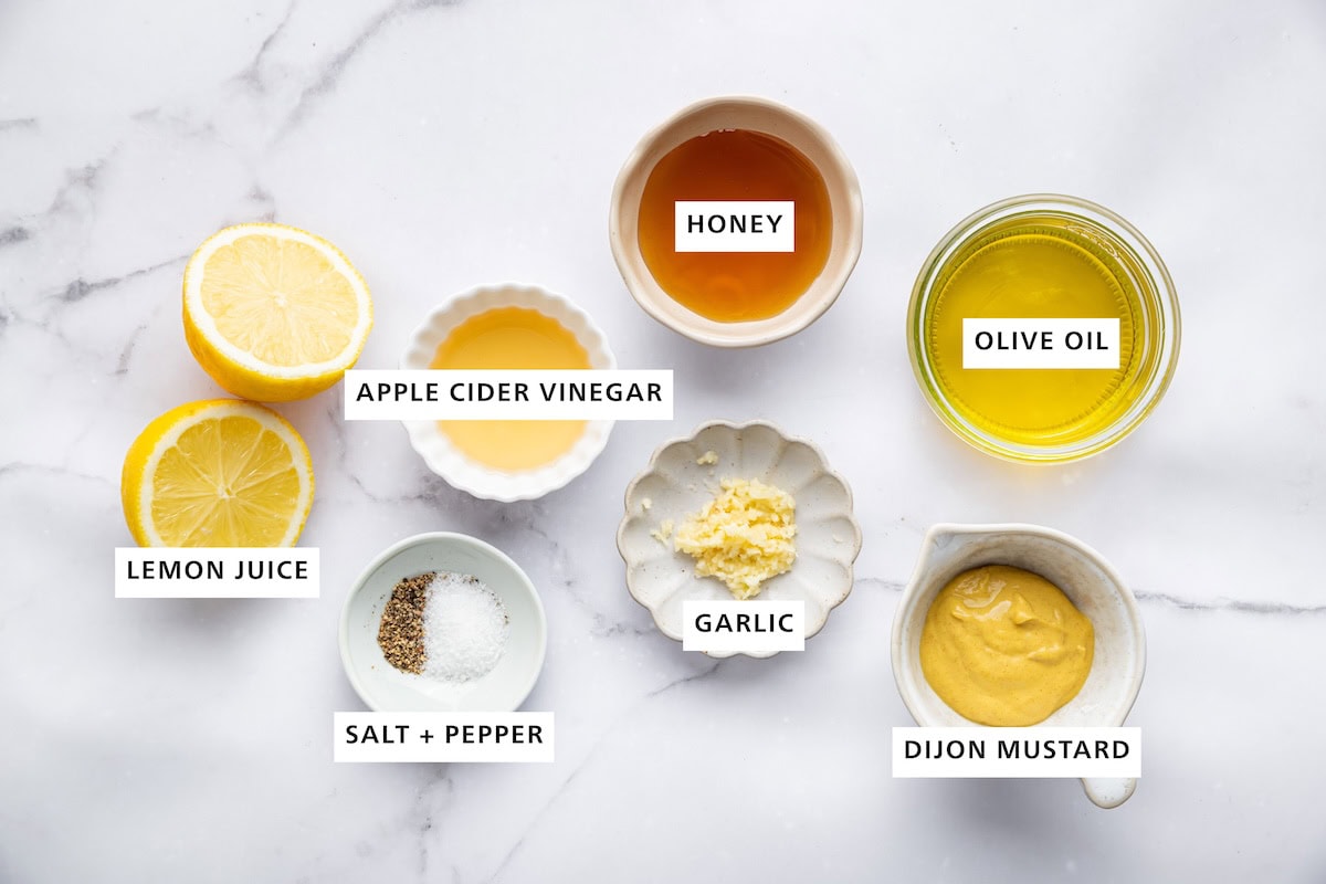 Ingredients measured out for honey mustard dressing: honey, olive oil, dijon mustard, garlic, salt, pepper, apple cider vinegar, and lemon juice.
