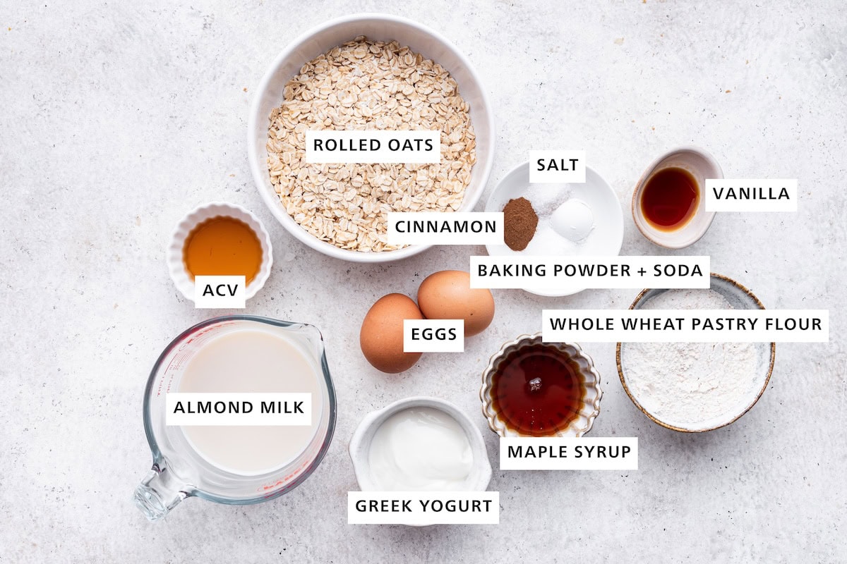 Ingredients measured out to make Overnight Oatmeal Pancakes: almond milk, vinegar, Greek yogurt, eggs, rolled oats, maple syrup, cinnamon, salt, baking soda, baking powder, whole wheat pastry flour and vanilla.