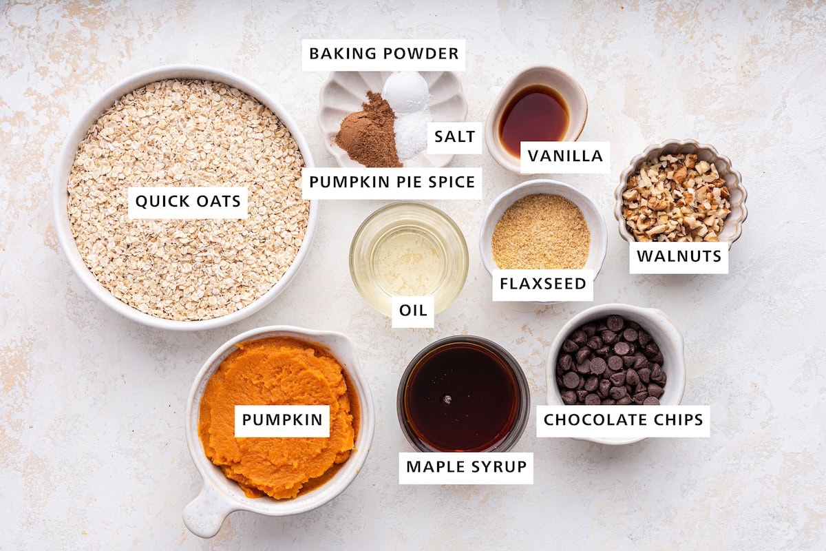 Ingredients measured out to make Pumpkin Oatmeal Bars: pumpkin, quick oats, pumpkin pie spice, sea salt, oil, baking powder, maple syrup, ground flaxseed, vanilla, chocolate chips and walnuts.