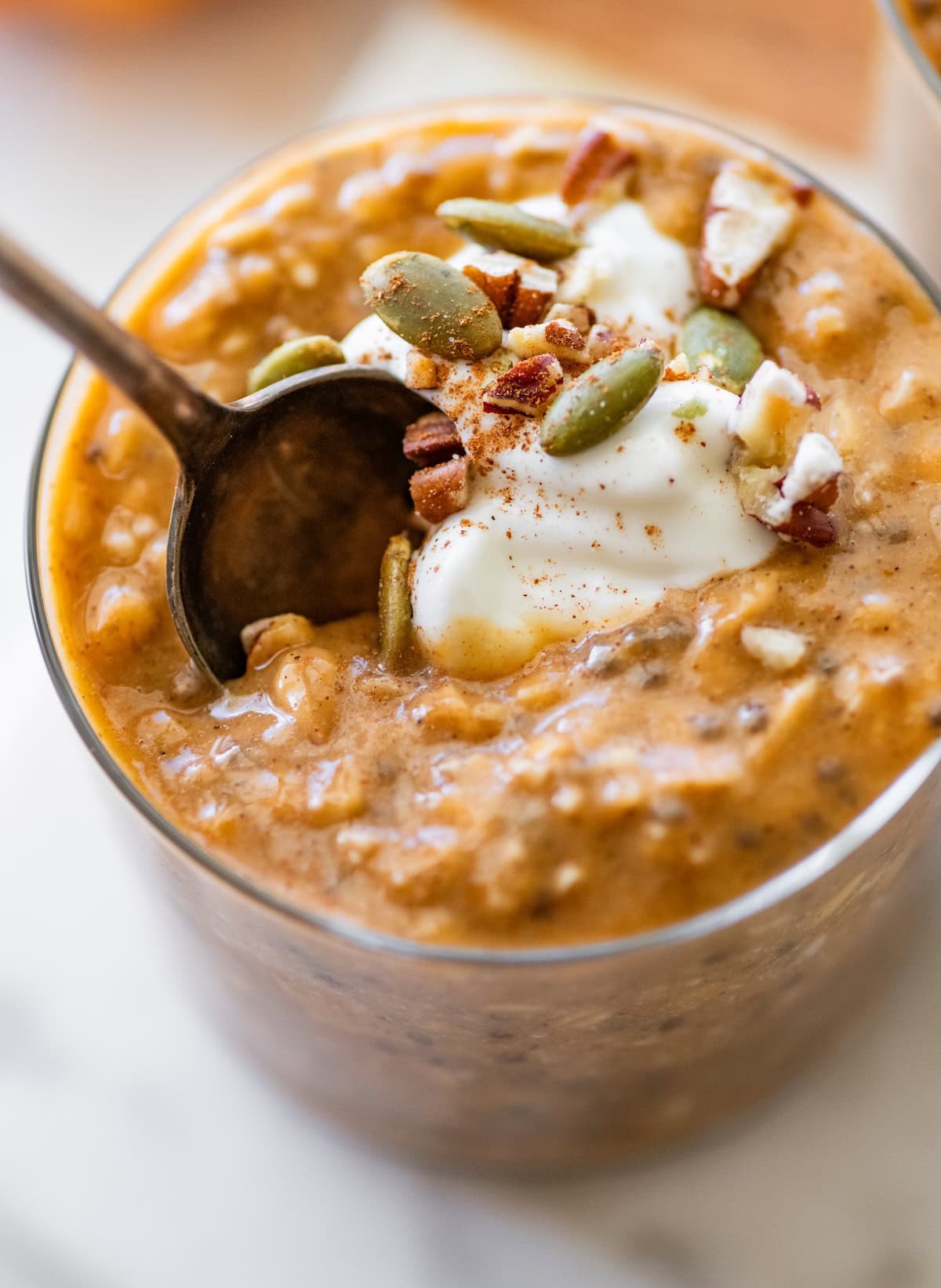 Pumpkin overnight oats in a glass cup with pumpkin seeds and crushed pecans.