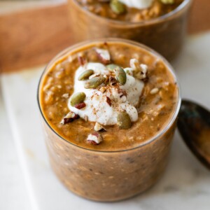 Pumpkin overnight oats in a glass cup topped with pumpkin seeds and pecans.