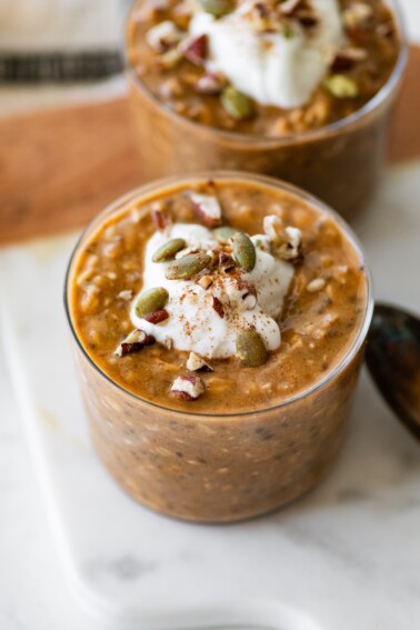 Pumpkin overnight oats in a glass cup topped with pumpkin seeds and pecans.